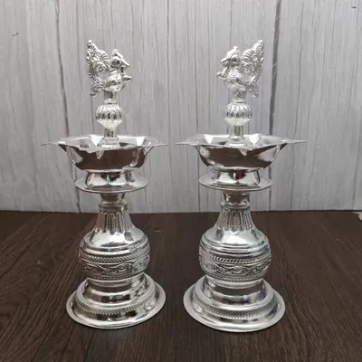 This pair of German silver Nakashi deepams stands tall and elegant. The intricate carving on the base and the peacock design on top make these standing lamps a stunning addition to any pooja room or doorway.