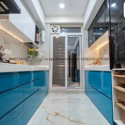 A full view of a vibrant blue parallel modular kitchen we designed in Ulwe. The glossy blue acrylic finish on the lower cabinets contrasts beautifully with the white overhead units and marble-patterned flooring, creating a long, seamless, and modern look.