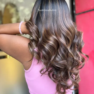 This side view highlights the placement of lighter balayage pieces that frame the face and add brightness. The blend of warm and cool brown tones creates a sophisticated look on these expertly styled curls.