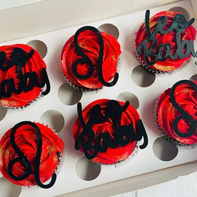 Celebrate a Leo's birthday with this bold and beautiful cupcake set. The rich chocolate cupcakes are topped with vibrant red buttercream, a sprinkle of gold glitter, and custom black acrylic toppers featuring the Leo zodiac symbol.