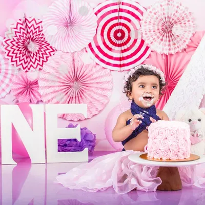 Her first taste of cake was a memorable one! This little girl is having a blast at her pink-themed cake smash, complete with a teepee and a 'ONE' sign.