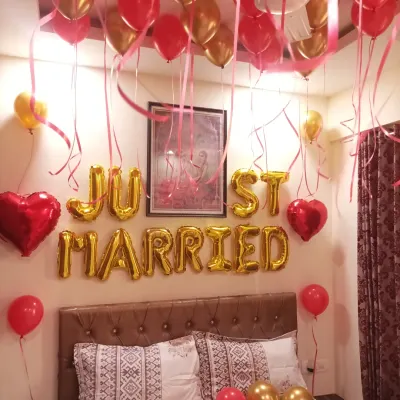 A classic 'Just Married' room decoration. The setup includes gold foil letter balloons over the bed, with red and gold balloons on the floor and ceiling.