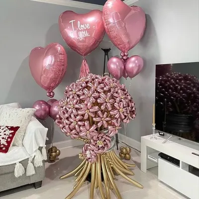 A truly unique gift: a giant flower bouquet made entirely of balloons. This stunning pink and gold creation is surrounded by heart-shaped foil balloons for a romantic gesture.