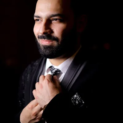 A classic, moody portrait of the groom adjusting his tie. The dramatic lighting creates a sophisticated and timeless look.