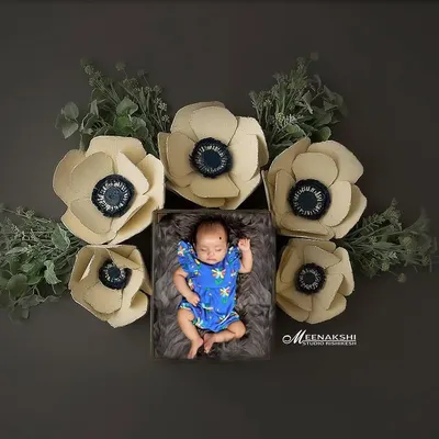 This is one of my signature newborn portraits. I designed this artistic, top-down setup in my studio, carefully placing the sleeping baby in a cozy box surrounded by large, soft paper flowers to create a beautiful, frame-worthy piece of art.