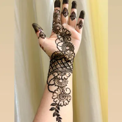 A classic Arabic-style henna design. This pattern features a vine of flowers and leaves that flows diagonally across the back of the hand, creating a very graceful and elegant look.