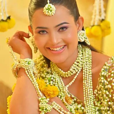 A radiant Haldi look. The makeup for this ceremony is all about a fresh, natural glow, complemented by beautiful floral jewelry. The skin looks luminous and healthy.