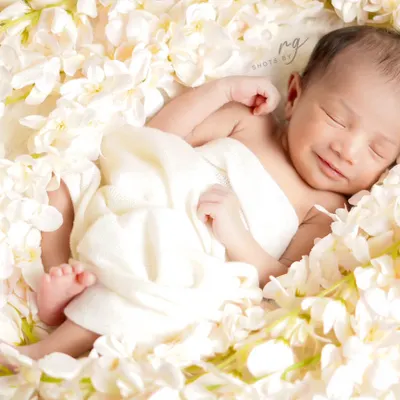 A happy little angel smiling in her sleep, surrounded by a bed of delicate white flowers. This is a perfect example of a pure and simple newborn portrait.