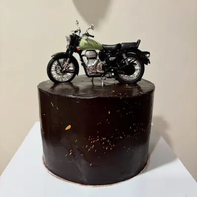 A tall 1.5kg Chocolate Ganache cake for a bike lover, topped with a detailed Royal Enfield model. The dark chocolate glaze with gold splatter gives it a sleek, masculine look.