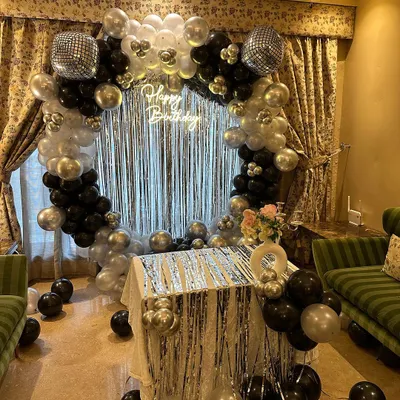 A full view of our popular disco-themed birthday decor. We use a circular balloon arch in black, silver, and white, a shimmery silver curtain, and a "Happy Birthday" neon sign to create the ultimate party vibe right in your living room.