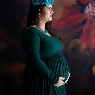 A beautiful profile shot of a mom-to-be in a dark green gown, wearing a blue floral crown. The painted backdrop adds an artistic touch to this serene portrait.
