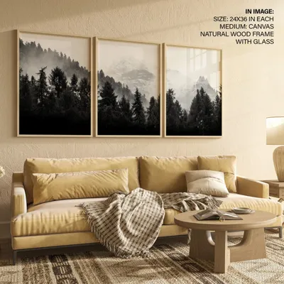 Create a dramatic and moody atmosphere with this set of three black and white forest photographs. The misty mountain scenes, framed in natural wood, work together to form a stunning panoramic landscape above a sofa.