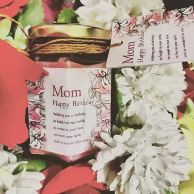 A beautiful birthday gift for a mother. This scented jar candle is customized with a "Happy Birthday Mom" message and presented here in a lovely floral arrangement.