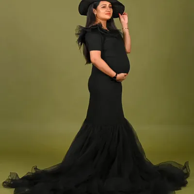 Sleek and sophisticated, this black mermaid gown features a fitted silhouette that flares into a dramatic tulle train. The look is completed with a stylish hat for a touch of classic glamour.