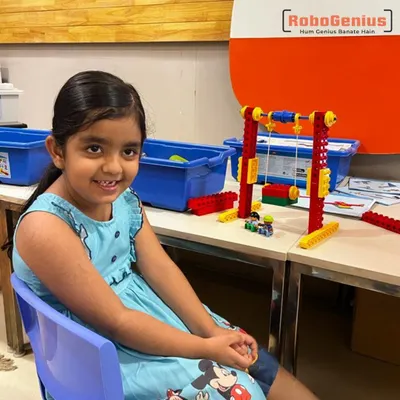 A kindergarten student from our summer camp sits with the functional LEGO swing set she built. This project helps young learners understand concepts of physics and structure in an intuitive, engaging way.