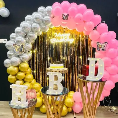 A vibrant and colorful birthday decoration setup. This image showcases a beautiful balloon arch with pink, silver, and gold, a shimmering backdrop, and our popular light-up 'HBD' letters.