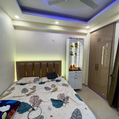 This bedroom includes a compact mandir unit placed neatly beside the wardrobe. The design features jali work and internal lighting.
