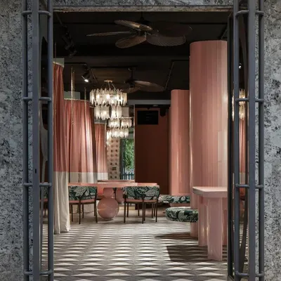The entrance to this fashion studio frames the interior like a stage. We used heavy, textured doors to create a sense of arrival, opening into a soft, curated world of pink tones, patterned floors, and dramatic chandeliers.