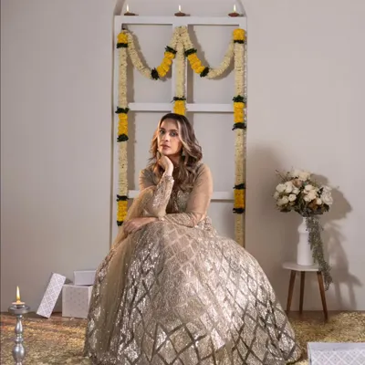 A full-length portrait from a festive studio shoot. The model's elegant pose in a sparkling lehenga, combined with the traditional decor of marigolds and diyas, creates a beautiful and celebratory image.