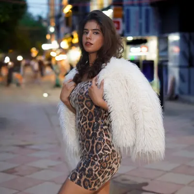 Capturing a bold street style look after dusk. The combination of a leopard print dress and a white faux fur jacket creates a statement against the blurred city lights.