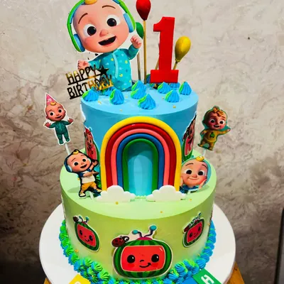 A vibrant two-tier Cocomelon cake, perfect for a first birthday. This colorful creation features JJ and his friends, a rainbow, and bright details from the popular show.