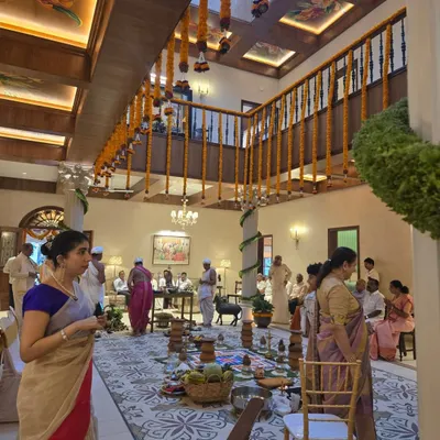 A glimpse into the family home of Sri Veerendra Hegde ji in Mangalore during a ceremony. The design features a double-height space with a coffer slab ceiling, traditional wooden railings, and a large, patterned rug.