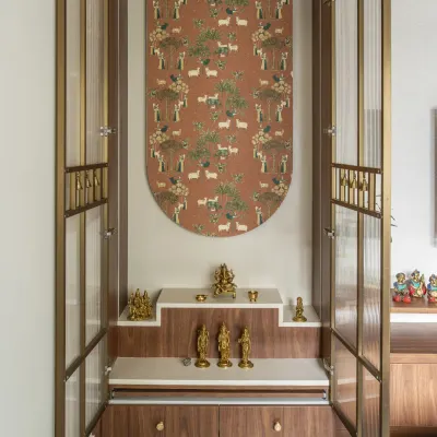 This elegant puja unit features a beautiful wallpaper backdrop with a traditional Indian motif. The unit itself has stepped platforms for idols and is enclosed by doors with fluted glass and metal accents.