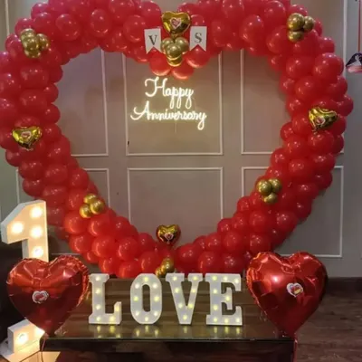 I created this grand heart-shaped balloon arch entirely with red balloons for a first-anniversary celebration. The setup is completed with a 'Happy Anniversary' neon sign, marquee 'LOVE' letters, and heart-shaped foil balloons.