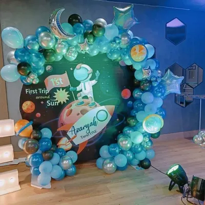 A "First Trip Around the Sun" space theme for a first birthday. The circular backdrop shows an astronaut on a rocket, surrounded by a balloon arch designed to look like the solar system.