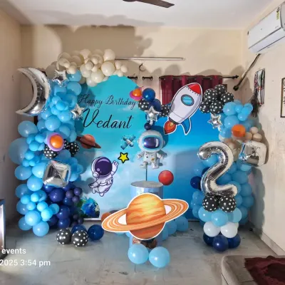 An out-of-this-world space theme birthday party for a second birthday. The setup is complete with a custom backdrop, balloon garlands, and cutouts of astronauts, rockets, and planets.