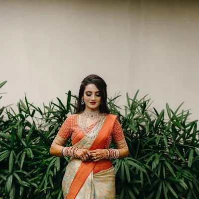 A beautiful solo portrait of a bride in her reception saree, looking down with a gentle smile. The simple background emphasizes her elegance and intricate jewelry.