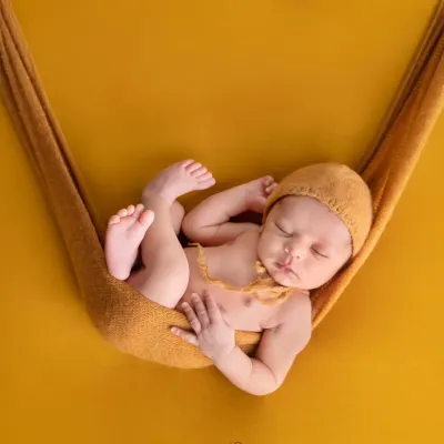 A classic newborn pose, with the baby sleeping peacefully in a mustard-colored sling against a matching backdrop. This highlights the simple, artistic style of my newborn photography.