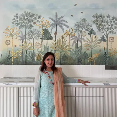 Art has the power to completely transform a room. My mother, Hansa Sewani, stands beside the 3D wall mural she created for this dining area. It took over 150 hours of handwork, using ceramic paste, acrylics, and gold leaf to bring this magical, nature-inspired scene to life.