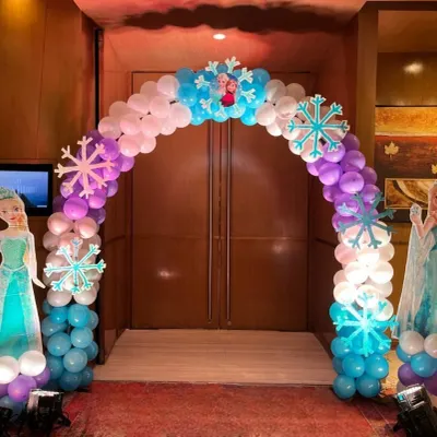 An inviting entrance arch we built for a Frozen-themed party. The structure is made of white, blue, and purple balloons with snowflake accents and is flanked by character standees, setting a magical tone right from the door.