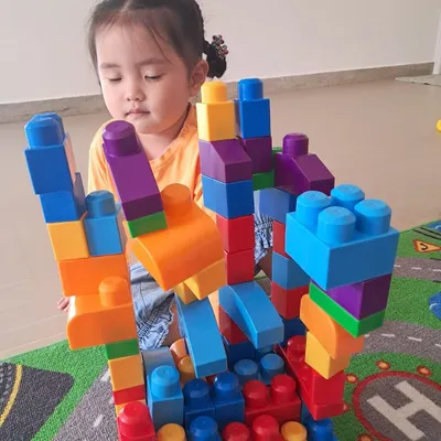 Using large, colorful blocks, this child builds a complex, multi-level structure. This type of open-ended play encourages imagination and develops foundational engineering skills.