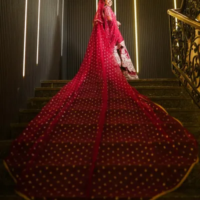 A breathtaking shot of the bride on a staircase, showcasing the magnificent trail of her red wedding lehenga. This kind of dramatic portrait makes a stunning album centerpiece.