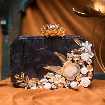 This black acrylic clutch is the definition of evening glamour. It's embellished with golden leaves, white 3D florals, and sparkling stones, all centered around a beautiful agate slice.