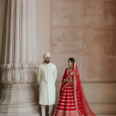 A regal portrait of a couple in their Sabyasachi wedding attire. The classic pose against the grand pillar at The Leela Palace in Bangalore creates a timeless, royal image.