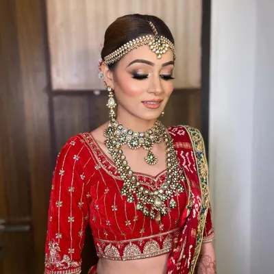 A classic red bridal look for Bhavika, featuring a flawless base and defined eyes to complement her traditional velvet lehenga and heavy jewelry.