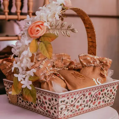 A beautifully arranged favor basket for a Roka ceremony. The basket itself features intricate traditional patterns, filled with monogrammed gift pouches for the guests to take home a piece of the celebration.