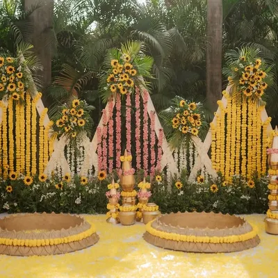This is a complete Haldi setup I designed, featuring a backdrop of marigold and sunflower curtains, traditional brass pots (matkas), and seating areas for the bride and groom, all tied together with a carpet of yellow petals.