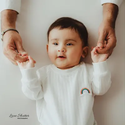 A sweet five-month milestone photo, with the baby lying down and holding his parent's hands. His direct gaze and cute expression are priceless.