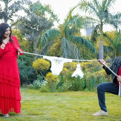 Having some fun during an outdoor shoot. This playful tug-of-war with a clothesline of baby clothes is a creative and lighthearted way to capture the couple's excitement.