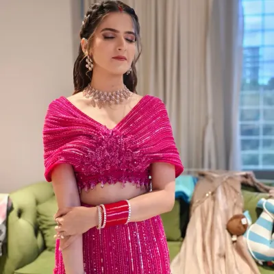 A soft and glowing makeup look for a Sangeet ceremony, with shimmery pink eyeshadow and a natural lip. The braided half-up hairstyle adds a touch of modern elegance to her vibrant pink outfit.