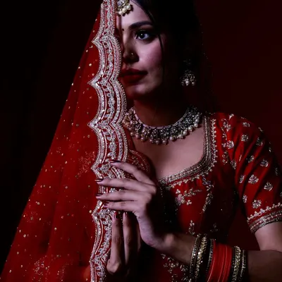 A classic bridal pose with the dupatta, creating a sense of mystery and elegance. This studio portrait uses focused lighting to draw attention to the bride's expressive eyes and the detailed embroidery of her red veil.