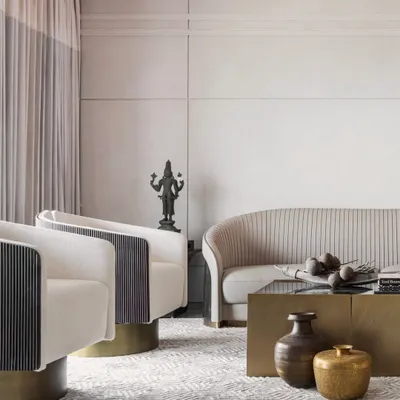 A study in textures and tones. This living space blends vintage brass accents and a traditional bronze statue with modern furniture silhouettes. The pleated sofa, swivel armchairs, and geometric rug create a layered, sophisticated aesthetic.