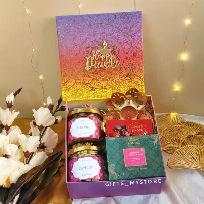 This vibrant purple and orange box opens up to reveal a curated selection of treats. It includes two jars of premium dry fruits, Lindt chocolates, TGL's Kashmiri Saffron Kahwa, and a beautiful lotus-shaped diya holder.