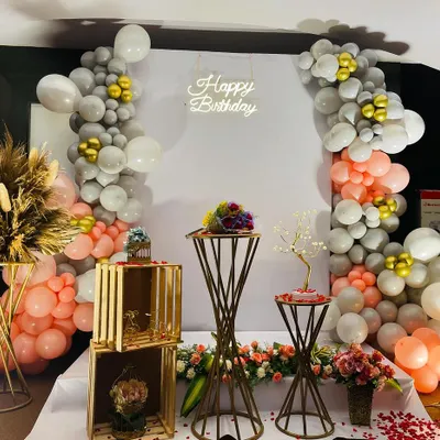 This chic setup is perfect for a sophisticated birthday celebration. It features a beautiful balloon arrangement in muted peach and grey tones, accented with gold and pampas grass, all centered around modern metallic pedestals.