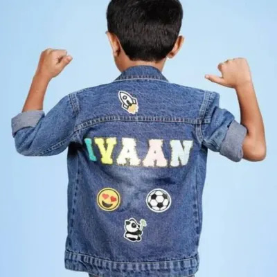 A custom denim jacket for a boy named "Iyaan," decorated with patches of a rocket, emoji, soccer ball, and panda.