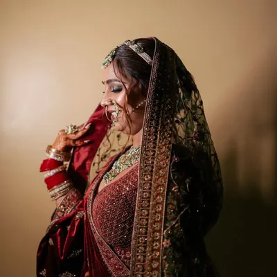 A side profile of a bride in a deep maroon velvet lehenga, showcasing the intricate embroidery and the complete look with a sheer dupatta. This is a classic choice for a winter wedding theme.